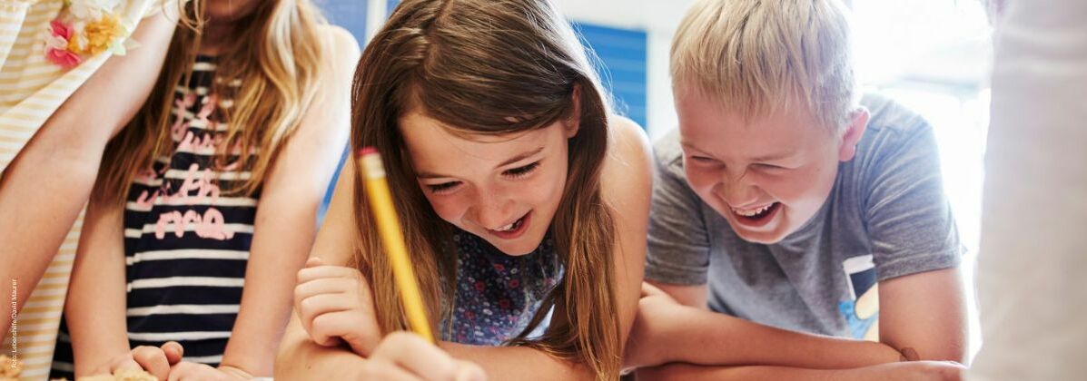 Mehrere lachende Kinder, die etwas schreiben oder zeichnen. Die Heilpädagogische Tagesstätte leistet einen zentralen Beitrag zur Entwicklung der Kinder