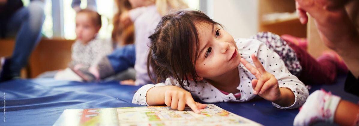 Ein kleines Mädchen mit einem Bilderbuch. Die Schulvorbereitende Einrichtung wird von Kindern besucht, die Unterstützung bei der Entwicklung brauchen.