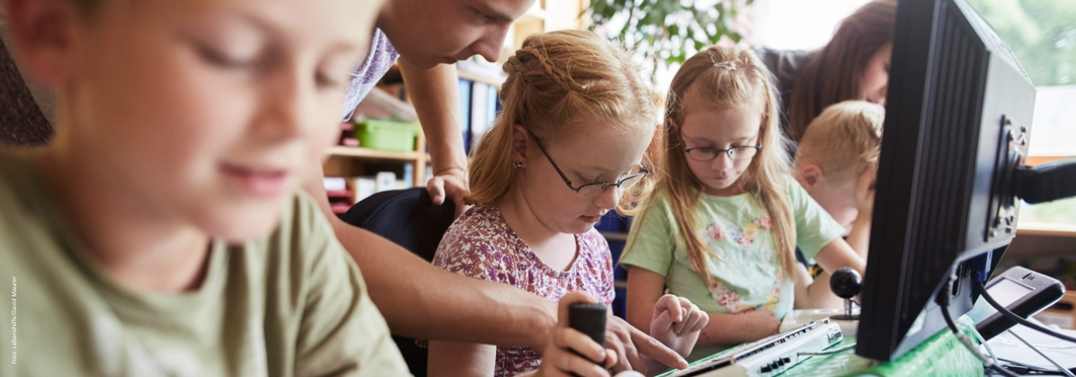 Kinder mit und ohne Behinderung sitzen vor Computern.