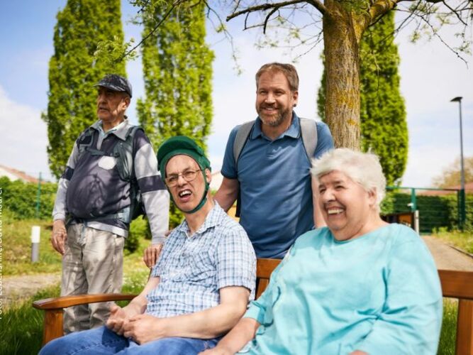 Menschen mit und ohne Behinderung auf einer Parkbank.